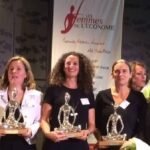 La remise de trophées avec trois plan, premier plan il y a trois trophées et un bouquet de fleur. Au second plan il ya les six femmes et au troisieme plan il y a le logo "Les femmes de l'économie"
